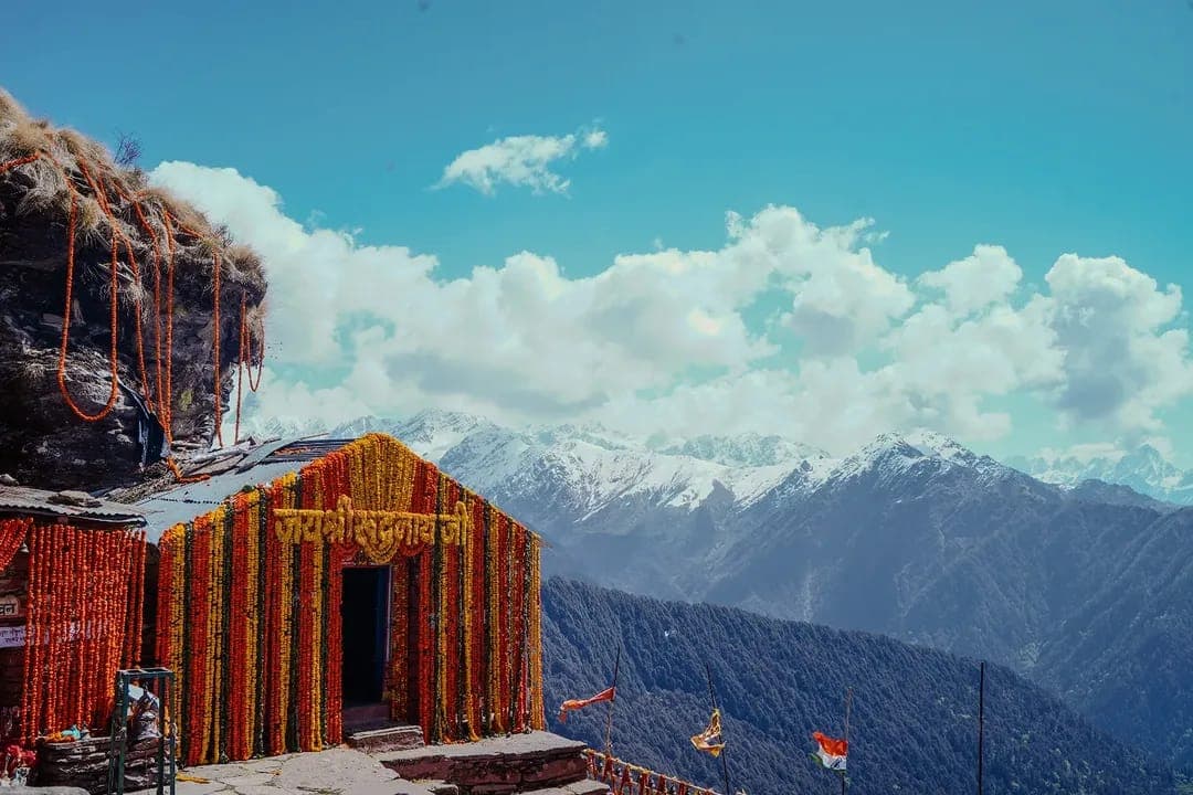 Orange rock-cut entrance of Rudranath Temple at 3,600m in Garhwal Himalayas with snow-capped peaks in the background